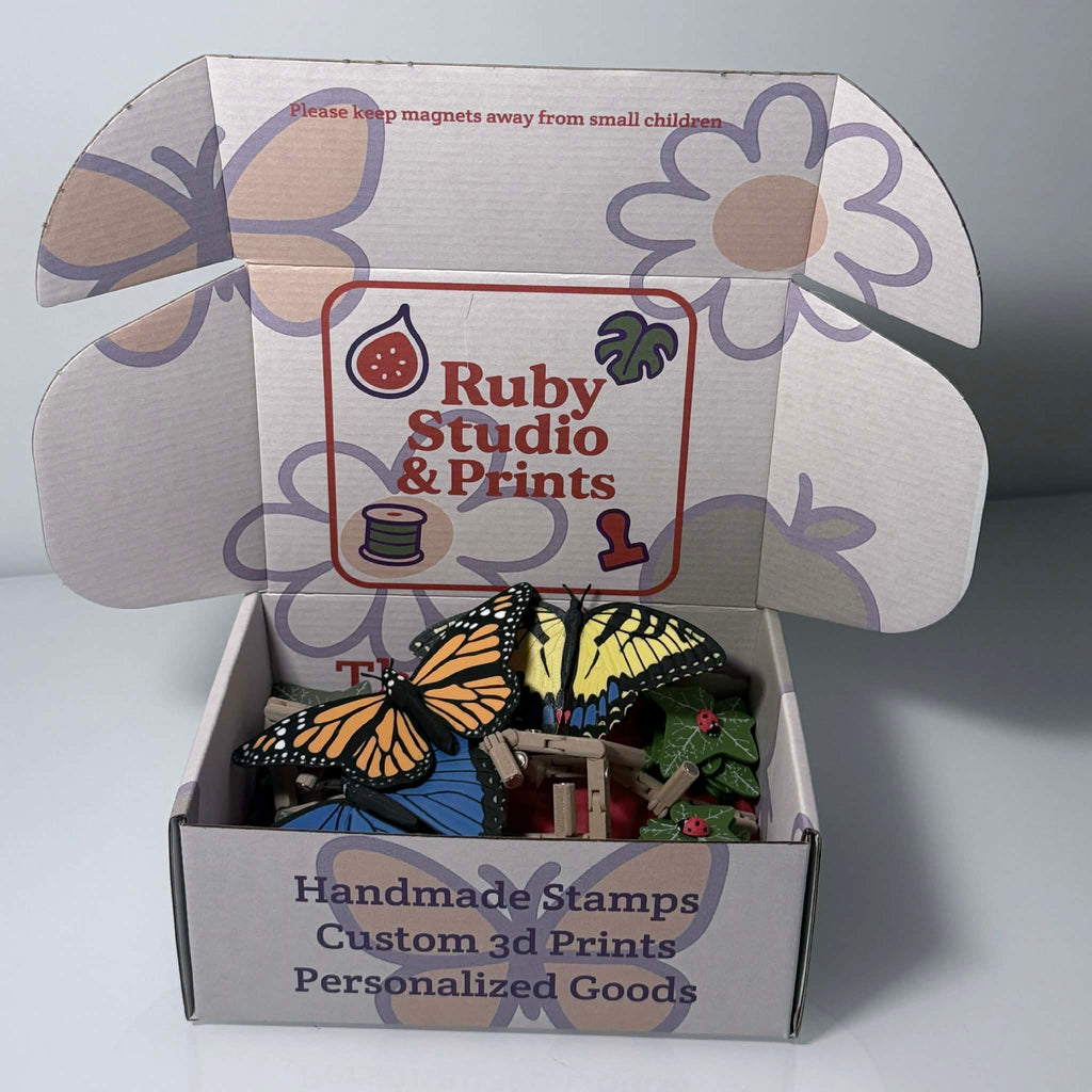 Branded box halfway opened with colorful butterflies, leaves, and ladybug magnets inside