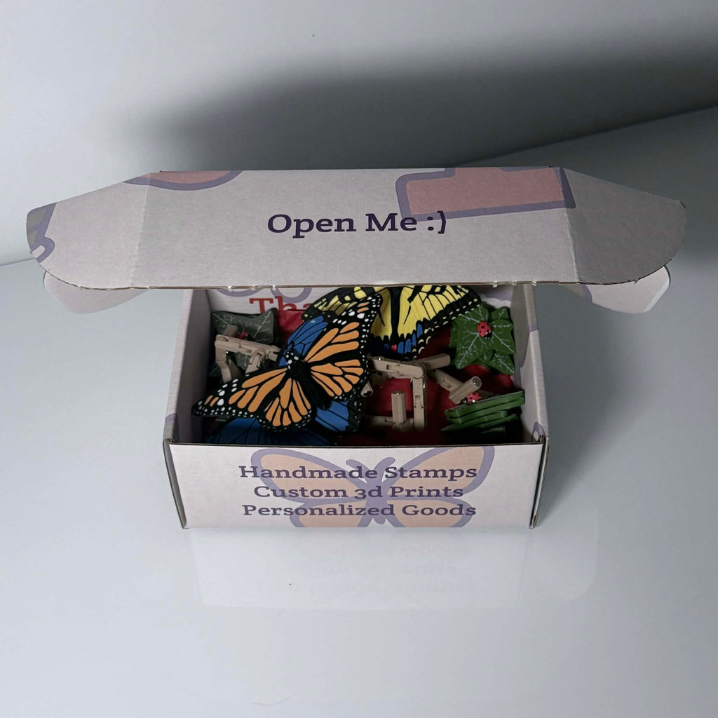 Branded box halfway opened with colorful butterflies, leaves, and ladybug magnets inside