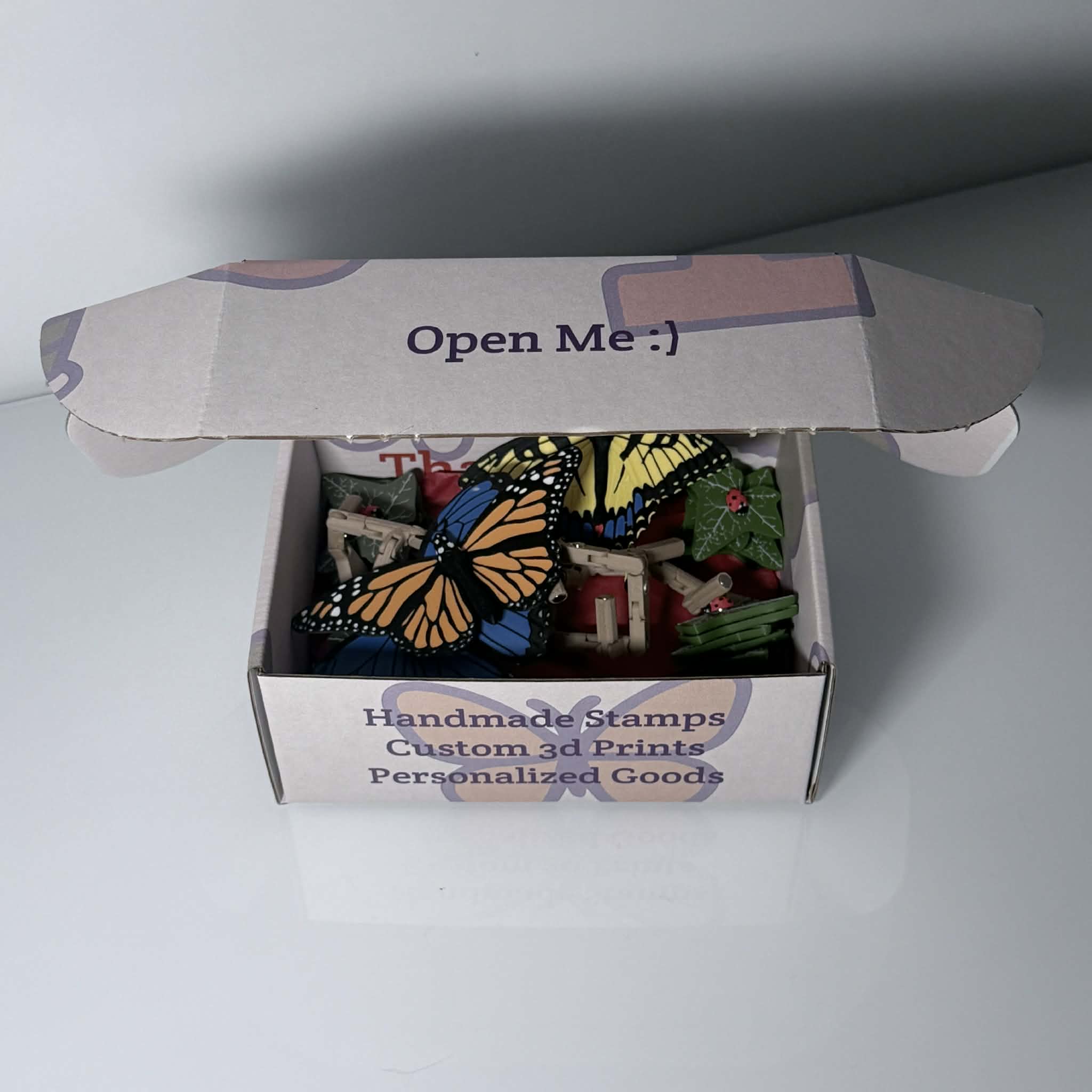 Branded box halfway opened with colorful butterflies, leaves, and ladybug magnets inside