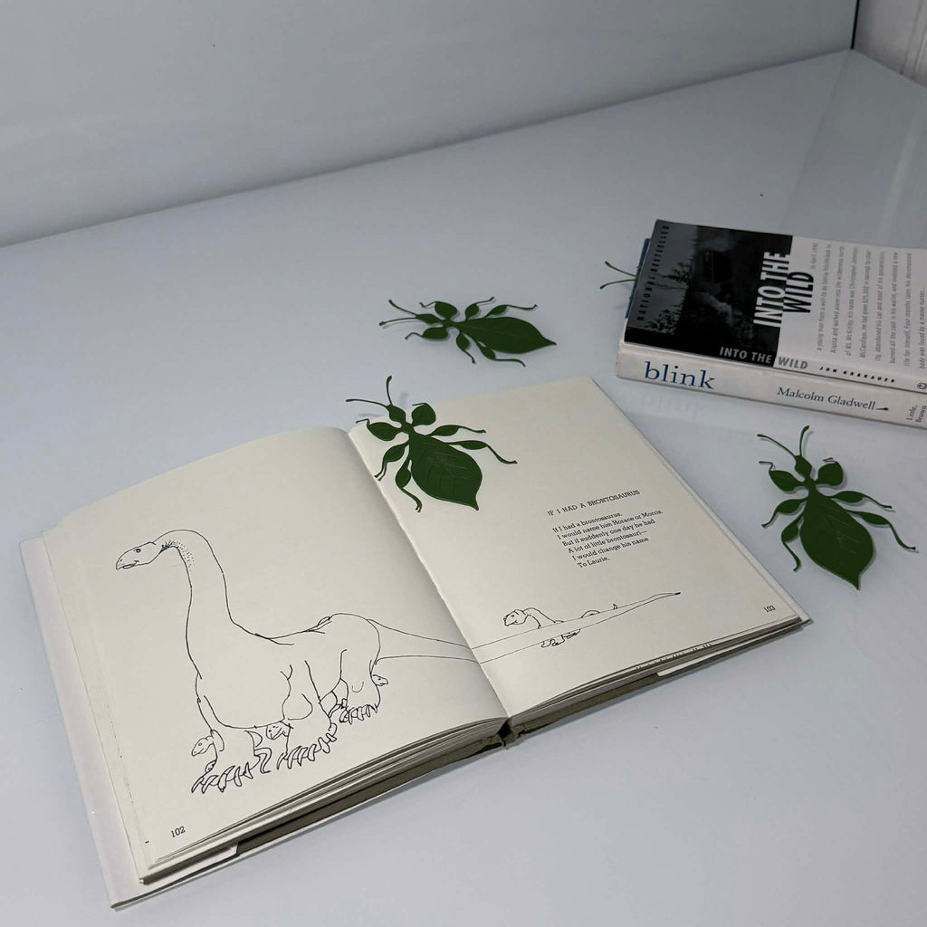 four leaf bug bookmarks on top of a book spread open and laying on the ground next to two books