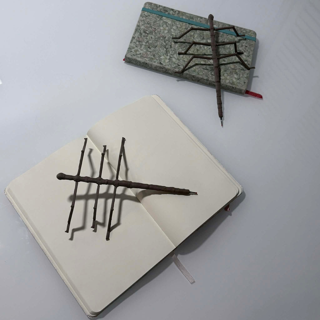 two stick bug pens laying on top of two notebooks, one open, one closed